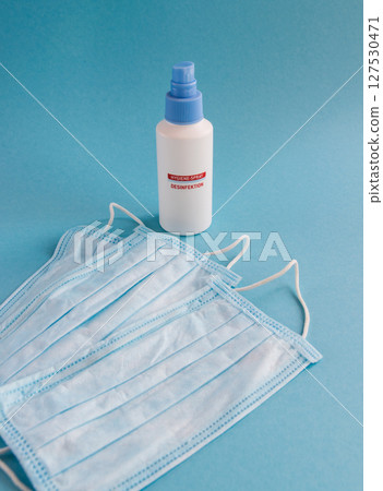 Desinfection spray and medical mask for hygiene on the blue background with place for text. Antibacterial, against pollution or virus protection. Covid-19 - coronavirus infection. Desinfection spray and medical mask for hygiene on the blue background with place for text. Antibacterial, against pollution or virus protection. Covid-19 - coronavirus infection. 127530471