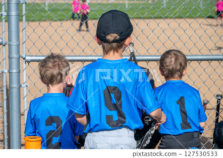 Row of youth T-ball boys sitting on the bench behind home plate waiting to bat. 127530533