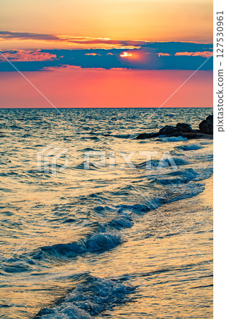 Sunset over sea and surf with waves, red sun through clouds, selective focus  127530961