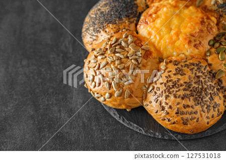 Bun with sunflower seeds, flax seeds, poppy seeds and baked cheese, on dark background, selective focus  127531018