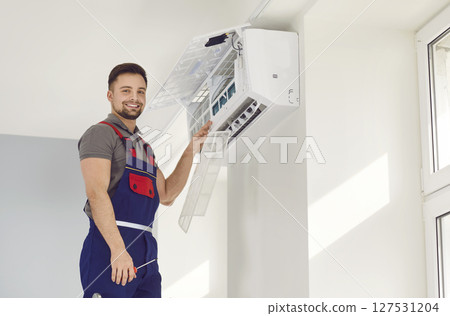 Portrait of electrician with screwdriver looking at camera and smiling maintaining air conditioner 127531204