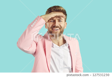 Happy young man in pink suit holds his hand on forehead above eyes and looks in distance 127531230