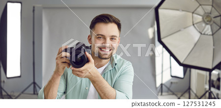 Happy smiling photographer holding a camera standing in professionally studio with light equipment. 127531245