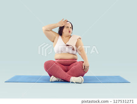 Tired funny overweight woman sitting on mat after fitness workout and wiping sweat off her forehead Tired funny overweight woman sitting on mat after fitness workout and wiping sweat off her forehead 127531271