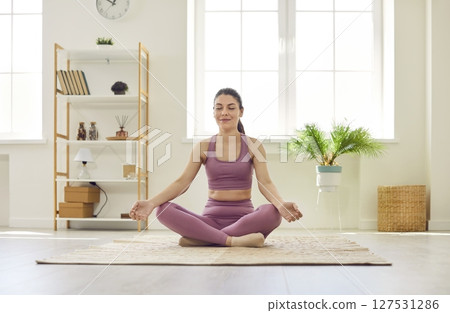 Portrait of a relaxed young woman doing yoga exercise at home sitting in lotus pose. Portrait of a relaxed young woman doing yoga exercise at home sitting in lotus pose. 127531286