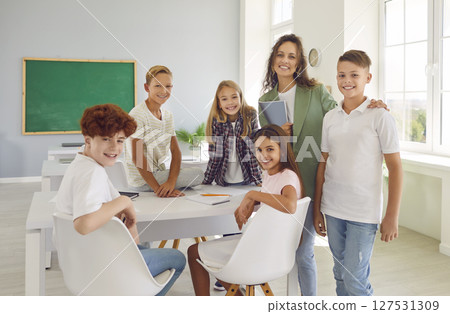 Happy school children with teacher standing in the classroom and looking at camera after a lesson. Happy school children with teacher standing in the classroom and looking at camera after a lesson. 127531309