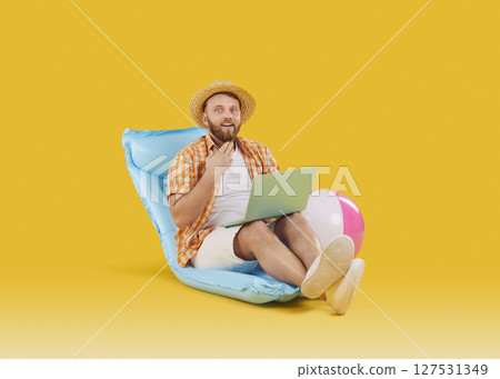 Funny man sitting on inflatable mattress booking tickets online on yellow background 127531349