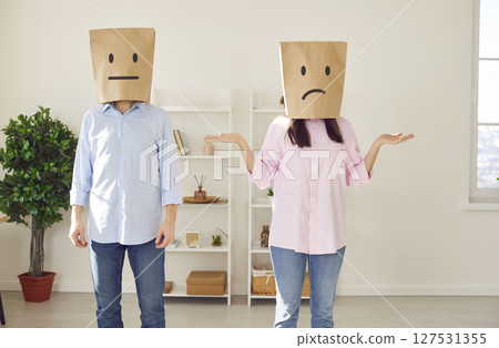Faceless man and woman with paper bags on head with confused faces standing in living room at home. Faceless man and woman with paper bags on head with confused faces standing in living room at home. 127531355