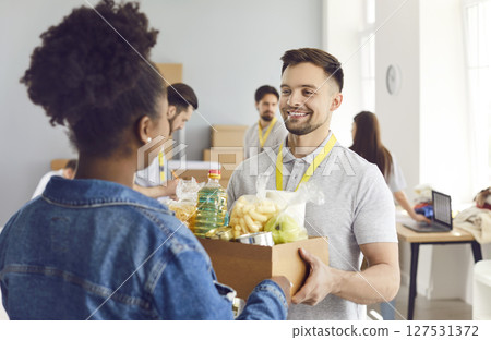 Young volunteer man giving food box to african american woman, charitable meal foundation 127531372