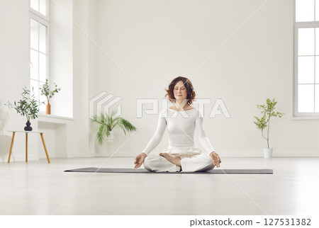 Beautiful yogi young woman relaxing, working out in white spacious room, resting after doing yoga 127531382
