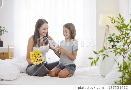 Preteen boy congratulates his mother on holiday by giving her bouquet of yellow tulips and card. 127531412