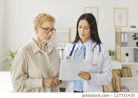 Doctor holding report file with appointment and prescribe treatment to a female patient in clinic. 127531430