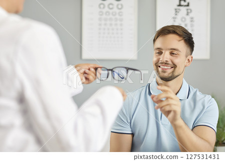 Optician, optometrist or ophthalmologist giving new glasses to young smiling man with vision problem 127531431