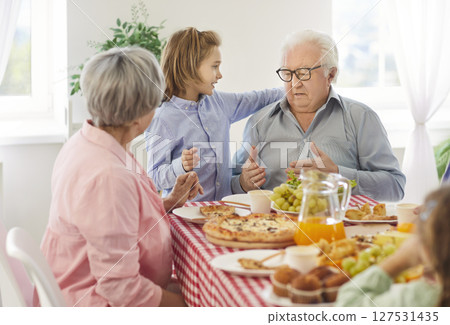 Grandpa and grandson talking while sitting at a dinner table together with other family members Grandpa and grandson talking while sitting at a dinner table together with other family members 127531435
