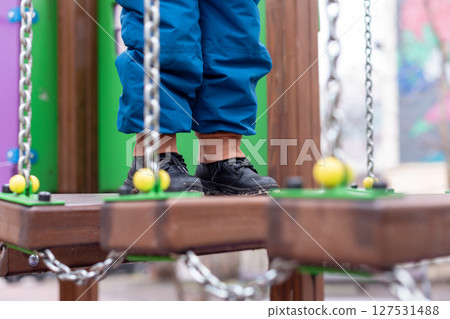Child walking on playground bridge with chains and colorful wooden elements. Child walking on playground bridge with chains and colorful wooden elements. 127531488