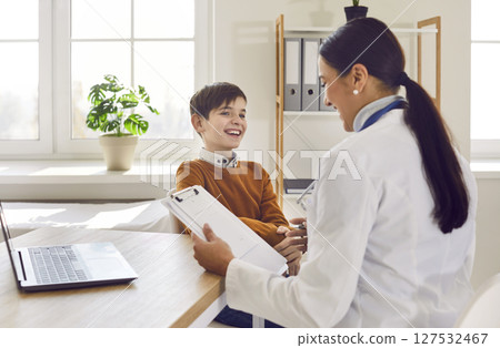 Smiling female pediatrician examining happy preteen boy patient in medical office 127532467