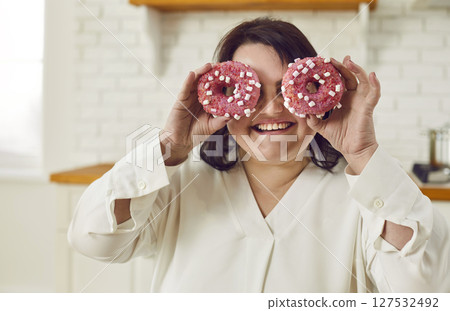 Close-up portrait of happy smiling plump fat plus size woman having fun with donut cakes on eyes. 127532492
