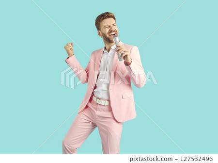 Happy man in a pink suit isolated on a blue background holding a microphone and singing a song Happy man in a pink suit isolated on a blue background holding a microphone and singing a song 127532496