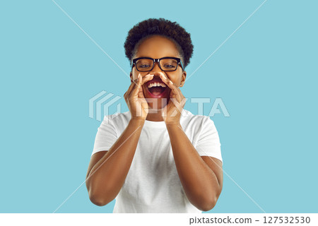 Funny woman holds her hands near her open mouth and speaks loudly against light blue background. 127532530