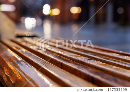 Raindrops glisten on a wooden bench in a cozy urban setting during a quiet evening 127533399
