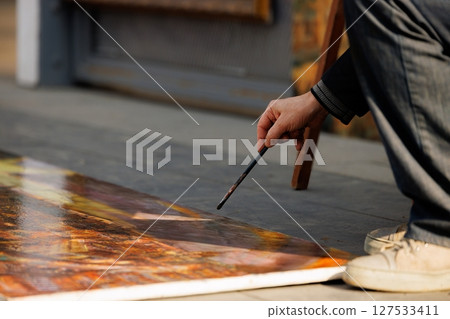 Artist meticulously creates a vibrant masterpiece on the floor during a sunny afternoon in the bustling square 127533411
