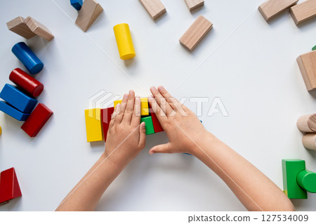 Child hands playing with colorful wooden blocks on white surface 127534009