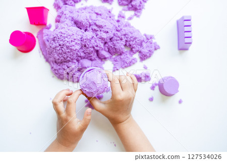 Child hands playing with purple kinetic sand and molds on white background 127534026