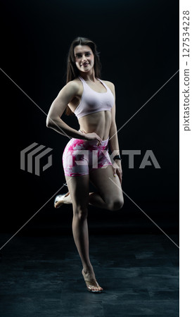 Athletic woman standing on black background, showing her fit body Athletic woman standing on black background, showing her fit body 127534228
