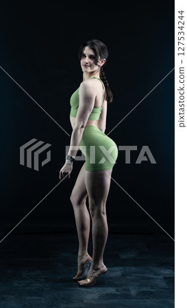 Athletic woman standing on black background, showing her fit body Athletic woman standing on black background, showing her fit body 127534244
