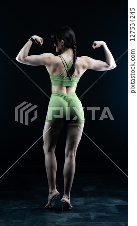 Athletic woman standing on black background, showing her fit body 127534245