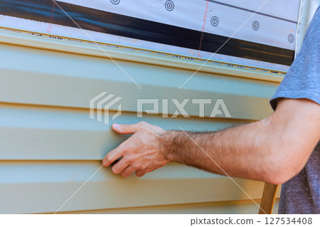 Homeowner installs new facade siding on house exterior during sunny day in suburban neighborhood 127534408