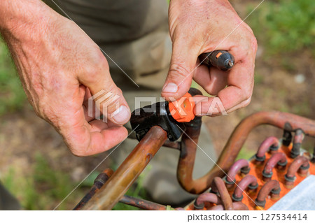 Hands connecting an orange fitting to copper pipe during maintenance 127534414