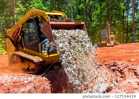 Heavy machinery operating at construction site for landscaping earth moving during works day in forested area Heavy machinery operating at construction site for landscaping earth moving during works day in forested area 127534419