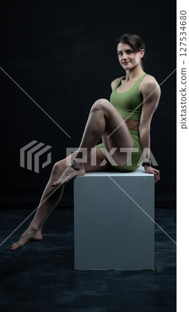 Athletic woman sitting on white cube in sportswear posing on black background 127534680