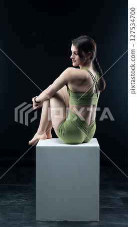 Athletic woman sitting on white cube in sportswear posing on black background 127534700