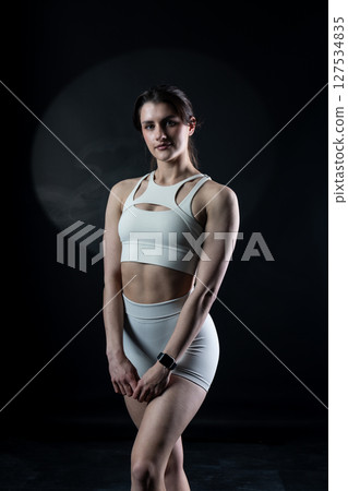 Athletic woman standing on black background, showing her fit body 127534835