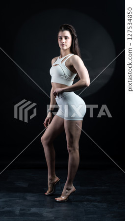 Athletic woman standing on black background, showing her fit body Athletic woman standing on black background, showing her fit body 127534850