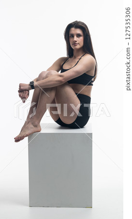 Young athletic woman posing on white cube in studio Young athletic woman posing on white cube in studio 127535306
