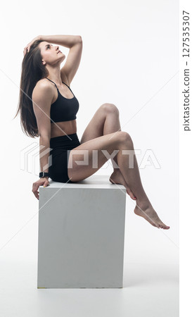 Young athletic woman posing on white cube in studio Young athletic woman posing on white cube in studio 127535307