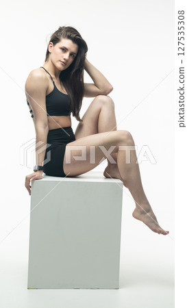 Young athletic woman posing on white cube in studio Young athletic woman posing on white cube in studio 127535308