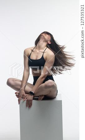 Young athletic woman posing on white cube in studio 127535321