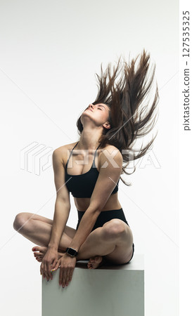 Young athletic woman posing on white cube in studio 127535325
