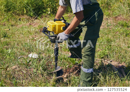 A man drills holes for a fence with a gas-powered auger A man drills holes for a fence with a gas-powered auger 127535524