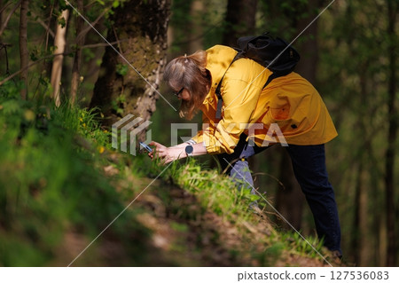 Exploring nature with curiosity in a vibrant yellow raincoat during a sunny day in the forest 127536083