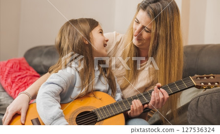 Mother teaching her daughter how to play guitar at home Mother teaching her daughter how to play guitar at home 127536324