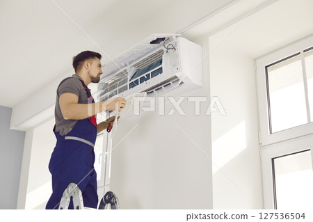 Male technician in uniform repairing air conditioner with screwdriver Male technician in uniform repairing air conditioner with screwdriver 127536504