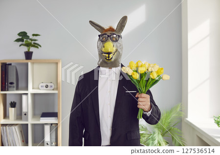 Funny man wearing animal donkey mask on head standing in office with a bouquet of tulip flowers. Funny man wearing animal donkey mask on head standing in office with a bouquet of tulip flowers. 127536514