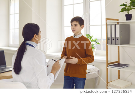 Female doctor talking with a child boy patient during medical examination in clinic. 127536534