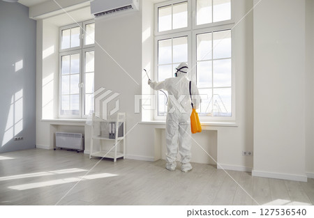 Pest control exterminator in protective suit spraying insecticide over windows in the house 127536540