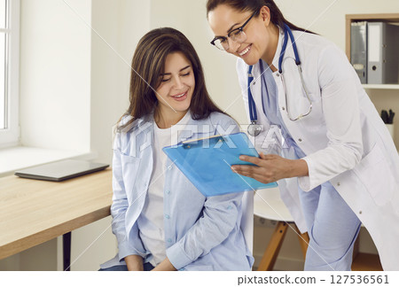 Friendly doctor showing report file with appointment to a young pregnant woman. Friendly doctor showing report file with appointment to a young pregnant woman. 127536561